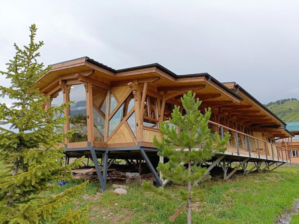 A wooden guesthouse in the Chon-Kemin Valley of Kyrgyzstan, surrounded by lush greenery and mountains.