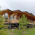 A wooden guesthouse in the Chon-Kemin Valley of Kyrgyzstan, surrounded by lush greenery and mountains.