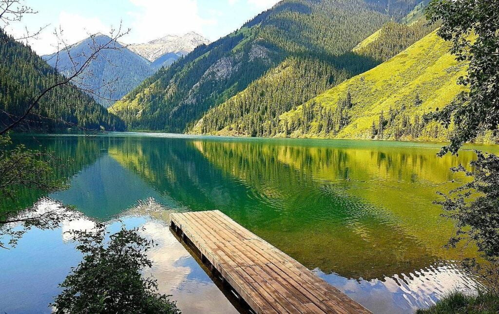 A picturesque view of Kolsay Lake in Kazakhstan with crystal-clear water reflecting the surrounding mountains and lush green forests.