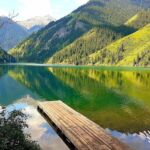 A picturesque view of Kolsay Lake in Kazakhstan with crystal-clear water reflecting the surrounding mountains and lush green forests.
