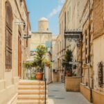 A charming narrow alley in the Old City of Baku, Azerbaijan, with historic buildings and potted plants lining the path under a bright blue sky.