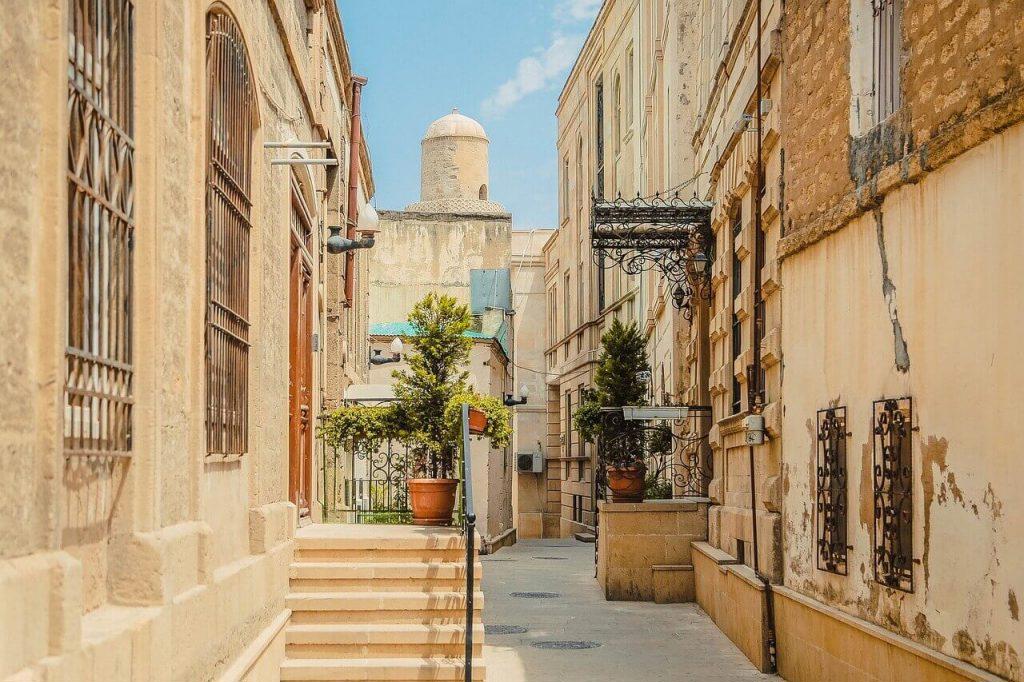 A charming narrow alley in the Old City of Baku, Azerbaijan, with historic buildings and potted plants lining the path under a bright blue sky.