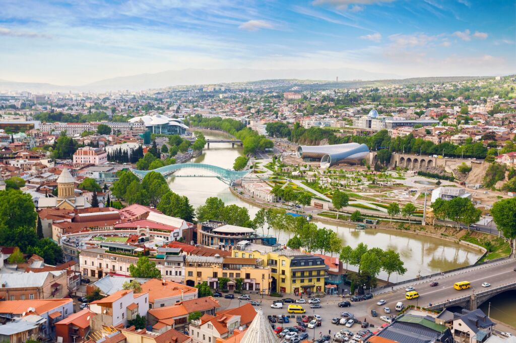 A panoramic view of Tbilisi, Georgia, showcasing the city's mix of modern and historic architecture, with the Kura River flowing through the heart of the city.