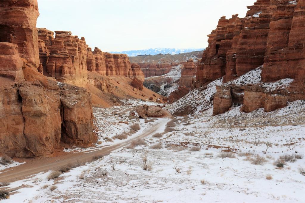 A snow-dusted Charyn Canyon in Kazakhstan during winter, featuring stunning red rock formations and a winding path through the canyon.