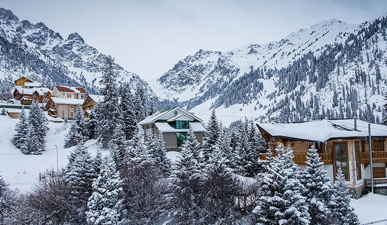 A cozy mountain resort nestled among snow-covered trees and mountains in Almaty, Kazakhstan, during the winter season.