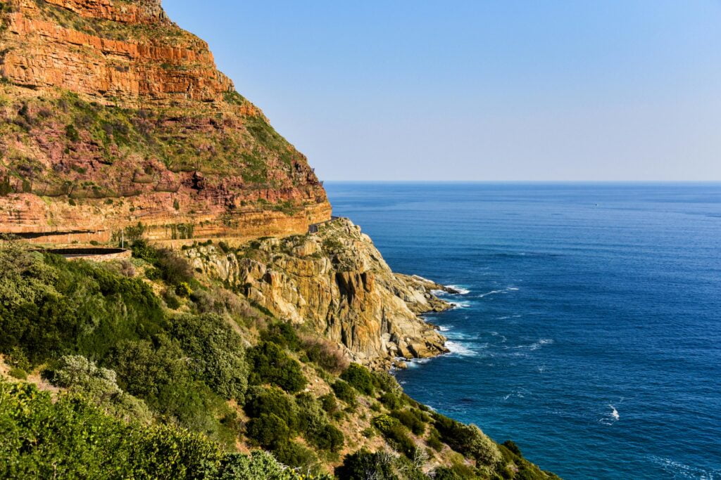 A stunning coastal cliff view along South Africa's Garden Route with rugged red cliffs and the blue ocean stretching into the distance.