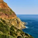 A stunning coastal cliff view along South Africa's Garden Route with rugged red cliffs and the blue ocean stretching into the distance.