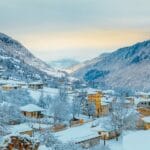 A picturesque snow-covered village nestled between the mountains in Georgia's Kazbegi region, surrounded by snowy landscapes and golden light.