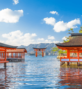 Itsukushima The floating torii gate of Itsukushima Shrine in Japan, set against a scenic bay with mountains in the background and traditional Japanese architecture on the water.