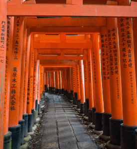 SHRINE OF FUSHIMI INARI The famous pathway of red torii gates at Fushimi Inari Shrine in Kyoto, Japan, leading visitors through a tranquil forest with kanji inscriptions on each gate.
