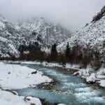 Snow-covered mountain landscape with a river flowing through Kyrgyzstan’s winter wilderness.