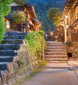 TSUMAGO VILLAGE A charming evening scene in Tsumago, Japan, with stone steps and wooden houses surrounded by greenery, evoking a sense of traditional Japanese village life.
