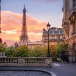 Eiffel Tower at sunset viewed from a charming Parisian street, surrounded by traditional architecture and warm hues.