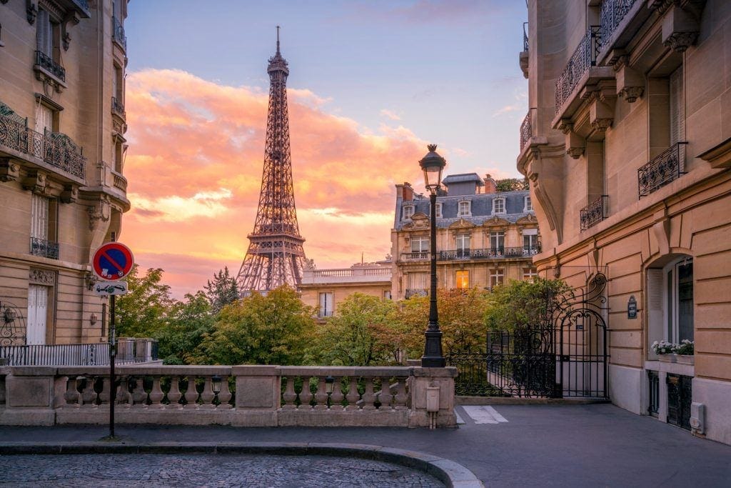 Eiffel Tower at sunset viewed from a charming Parisian street, surrounded by traditional architecture and warm hues.