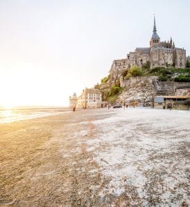 Mont Saint-Michel Abbey Close-up view of Mont Saint-Michel Abbey, perched atop the island, featuring its Gothic architecture, tall spires, and intricate stonework, with the surrounding tidal waters reflecting the abbey's grandeur.