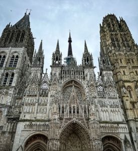 Rouen Cathedral Detailed view of Rouen Cathedral in France, showcasing its impressive Gothic architecture, intricate façade, and towering spires, with sunlight casting shadows on the ornate stonework.