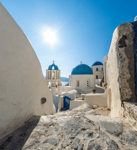 Santornini Iconic view of Santorini, Greece, with its white-washed buildings and blue-domed churches perched on cliffs, overlooking the caldera and the crystal-clear waters of the Aegean Sea, under a bright blue sky.