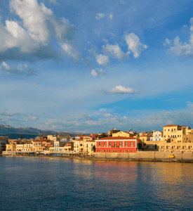 Chania Crete Charming view of the Venetian harbor in Chania, Crete, with colorful buildings, a lighthouse, and crystal-clear waters under a bright blue sky.