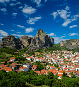 Kalampaka Village Scenic view of Kalampaka village in Greece, nestled at the base of towering rock formations, with traditional stone houses and a backdrop of lush green landscapes.